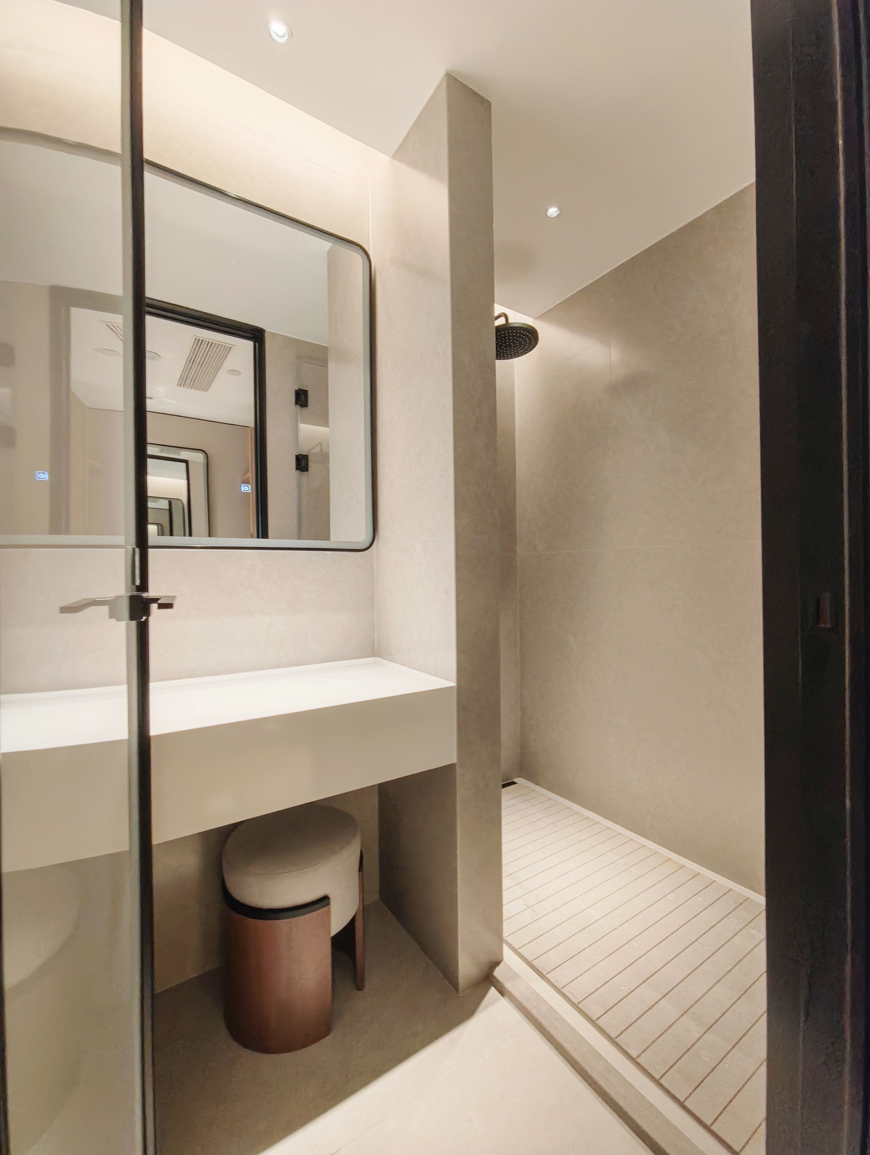 Un baño moderno con un espejo grande, una ducha y un tocador con un taburete.