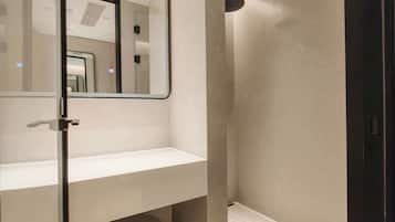 A modern bathroom with a large mirror, a shower, and a vanity with a stool.