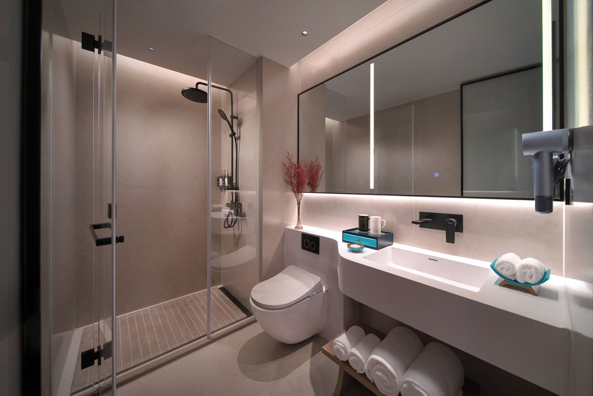 A modern bathroom with a glass-enclosed shower, a toilet, a sink with a mirror, and neatly rolled towels.
