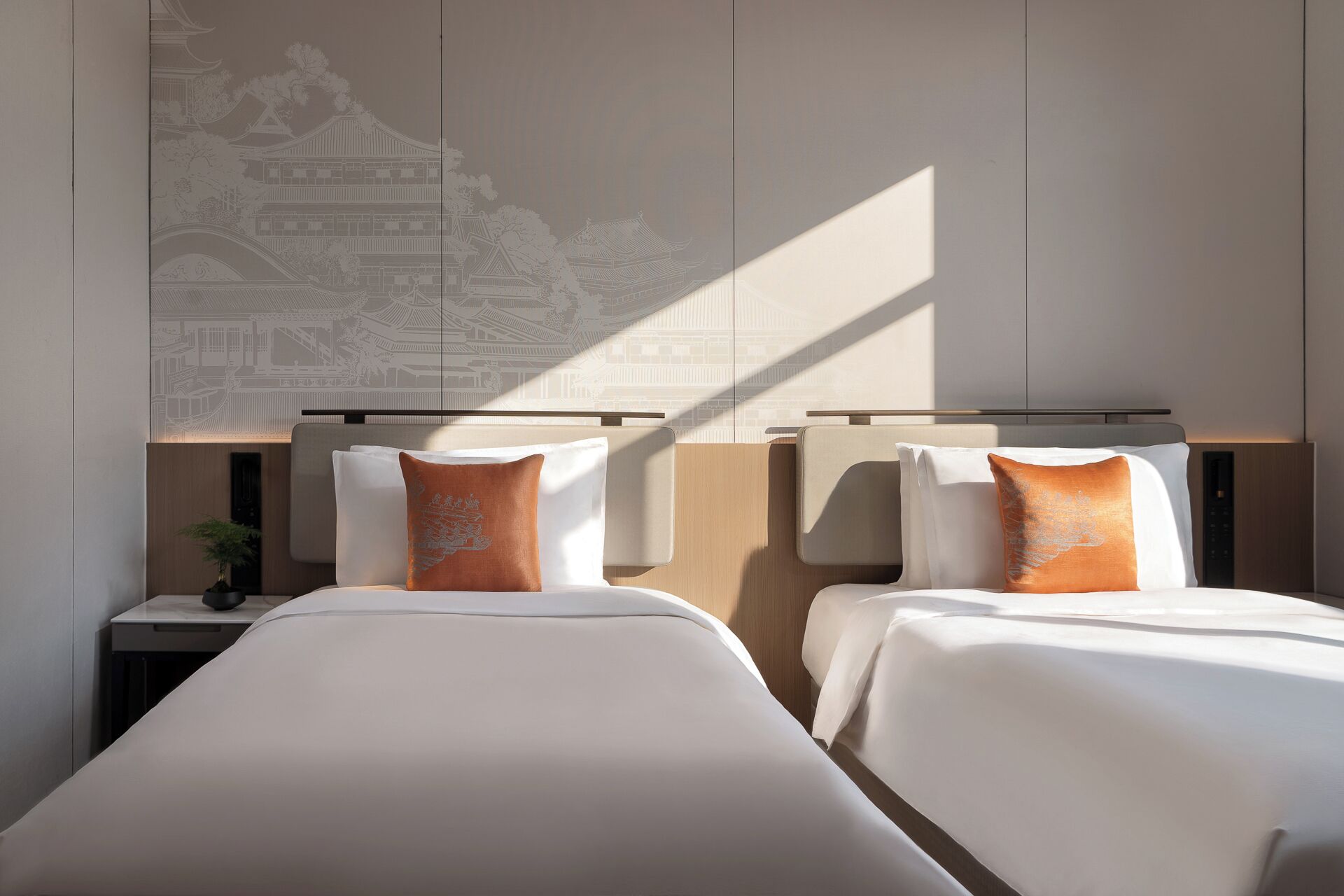 Habitación de hotel con dos camas, una mesita de noche con lámpara y una pared con un diseño arquitectónico discreto.