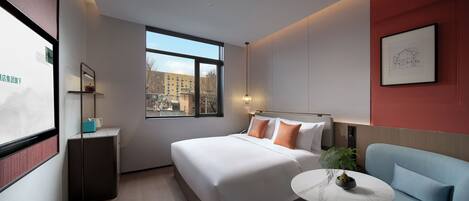 A modern hotel room with a large bed, a small table with a plant, a blue armchair, and a window with a city view.