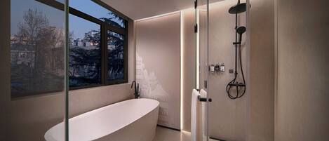 Un baño moderno con una bañera independiente, ducha con cerramiento de vidrio y vistas a un paisaje urbano a través de amplios ventanales.