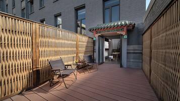 Una terraza de madera con dos sillones, una mesita y una entrada decorativa con techo de azulejos.