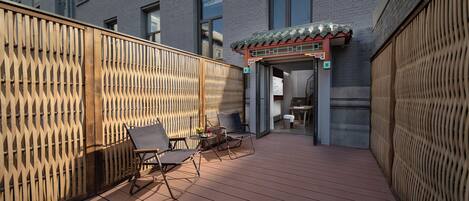 A wooden deck with two lounge chairs, a small table, and a decorative entrance with a tiled roof.