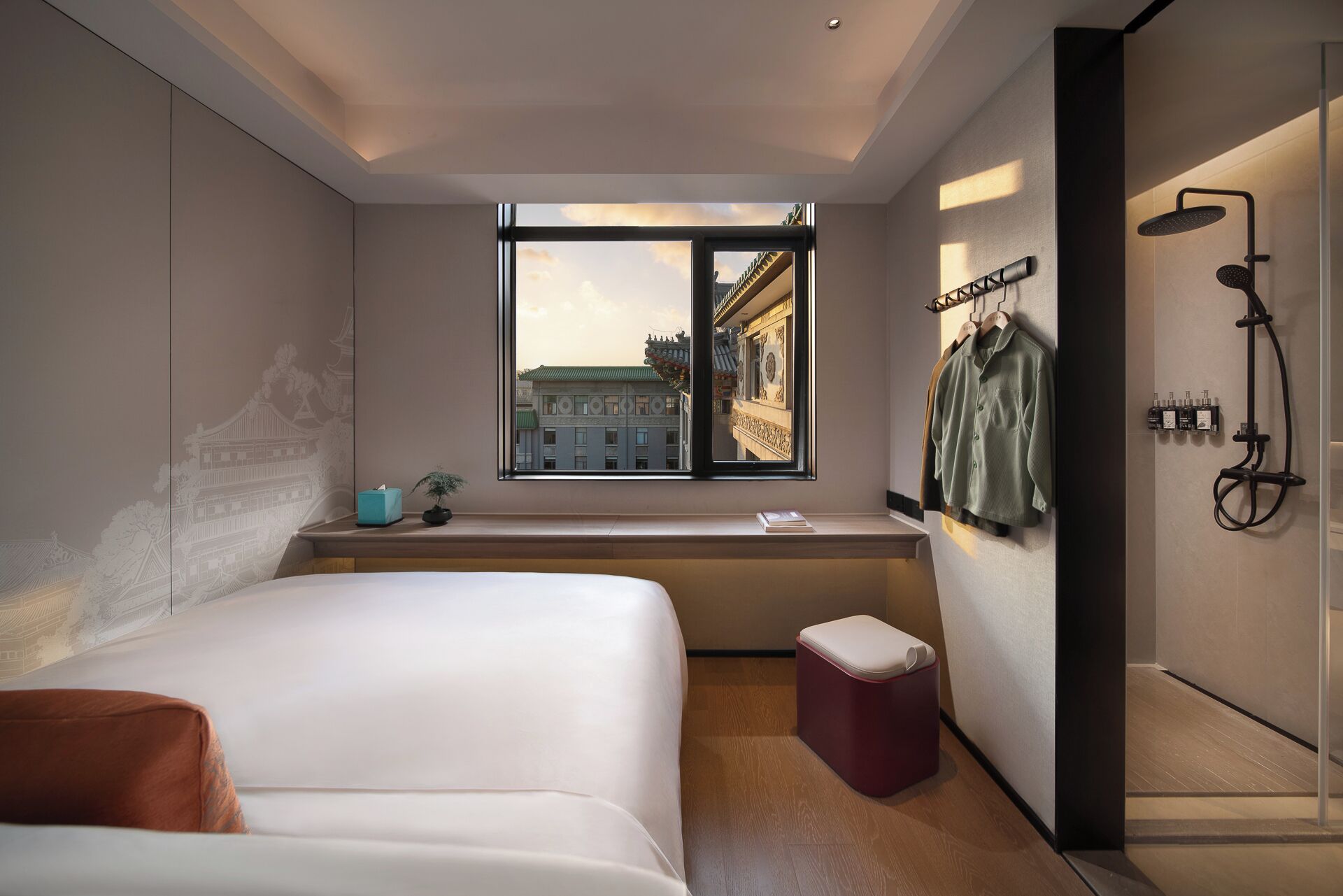 A modern hotel room with a large bed, a small bedside table, a window with a view of buildings, and a shower area.