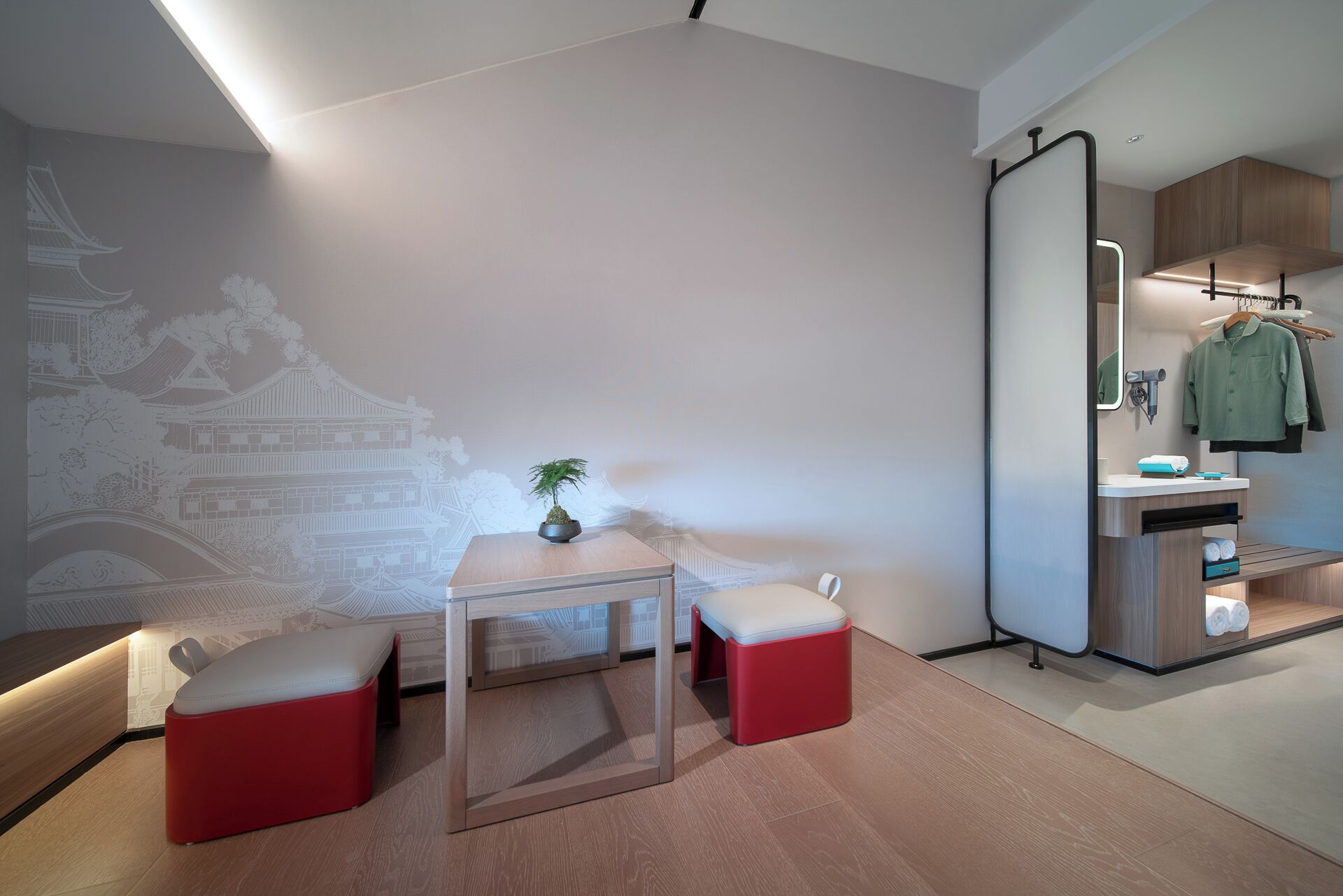 A modern room with a minimalist design, featuring a wooden table, two red ottomans, a potted plant, and a wall mural.
