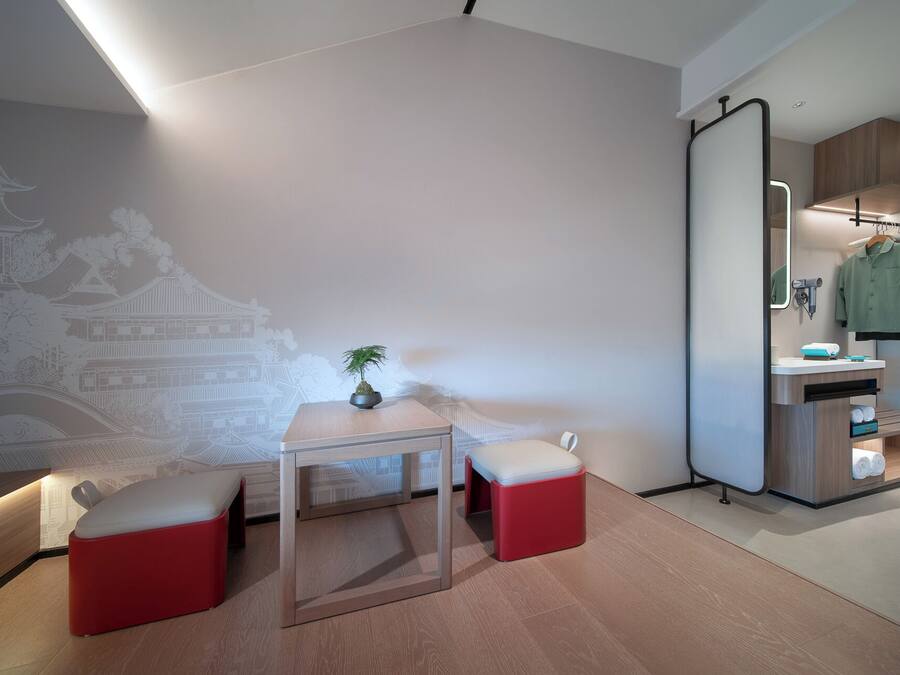A modern room with a minimalist design, featuring a wooden table, two red ottomans, a potted plant, and a wall mural.