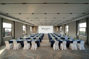 A conference room with rows of tables and chairs, a large screen at the front, and large windows on the sides.