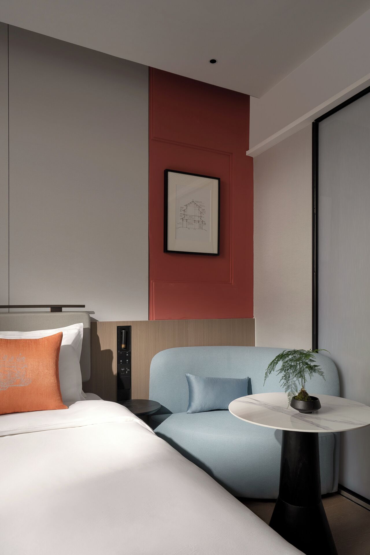 A modern hotel room with a bed, a sofa, a small table with a plant, and a framed picture on the wall.