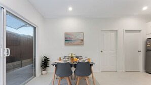 A dining area with a table set for four, a potted plant, and a painting on the wall. - Stylish 2BR Retreat | Walk to Dining & Transport (Hurstville)