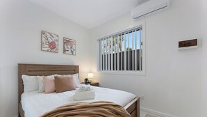 A bedroom with a wooden headboard, white bedding, a brown throw blanket, and two wall-mounted artworks. - Stylish 2BR Retreat | Walk to Dining & Transport (Hurstville)