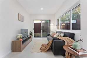 Una sala de estar moderna con un televisor de pantalla plana, un sofá, una mesa de centro y una estantería.