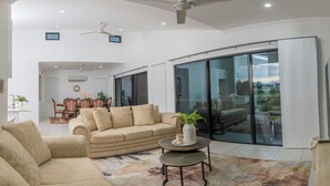 Ein geräumiges Wohnzimmer mit einem beigen Sofa, einem Couchtisch und Blick durch große Schiebeglasfenster auf einen Außenbereich.