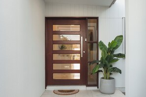 A brown wooden door with glass panels and a potted plant beside it. - Welcome River View Haven, your stylish retreat in the heart of Townsville! (Oonoonba)
