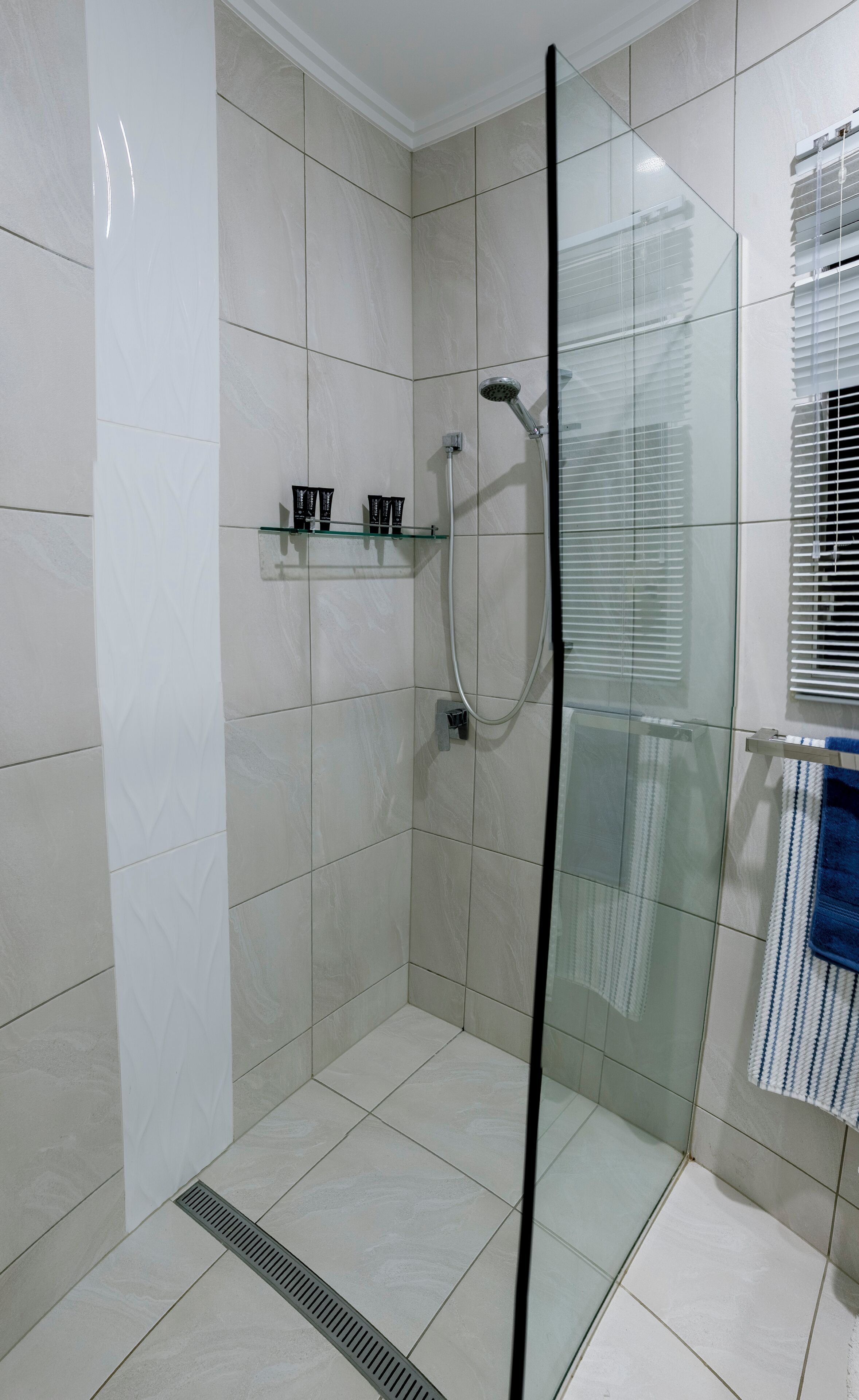 Un baño moderno con cabina de ducha de vidrio, azulejos blancos y un perchero con una toalla azul.