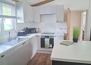 Cocina compacta con armarios blancos, microondas integrado, lavavajillas y un lavabo.