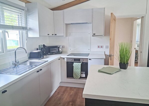 A compact kitchen with white cabinets, a built-in microwave, a dishwasher, and a sink.