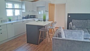 Una cocina moderna con una isla central, taburetes de bar, un sofá gris y techo de madera.