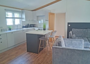 A modern kitchen with a central island, bar stools, a grey sofa, and a wooden ceiling.