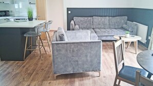 Un espacio habitable moderno con un sofá gris, una mesita redonda y una cocina con microondas y una planta.