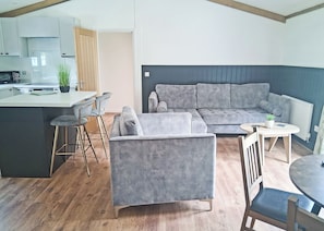A modern living space with a grey sofa, a small round table, and a kitchen area with a microwave and a plant.