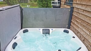 A hot tub with a control panel, surrounded by a wooden deck and a concrete wall.