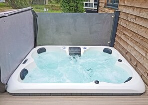 A hot tub with a control panel, surrounded by a wooden deck and a concrete wall.