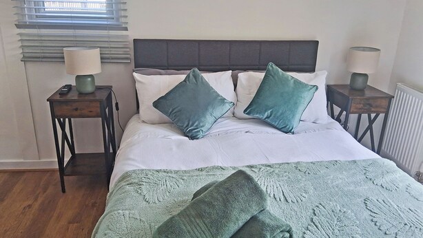 A bed with a grey headboard, two bedside tables with lamps, and a window with blinds.