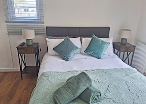A bed with a grey headboard, two bedside tables with lamps, and a window with blinds.