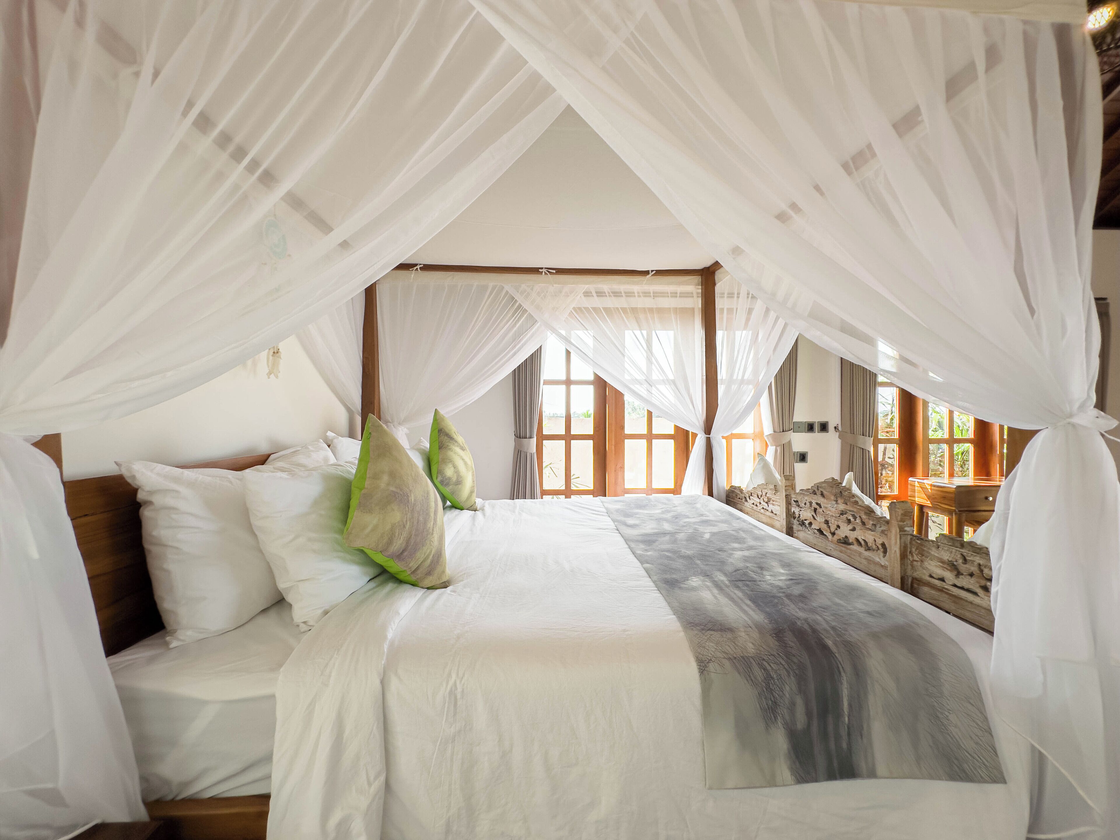 A bedroom with a canopy bed, wooden headboard, and a view of the outdoors through large windows.