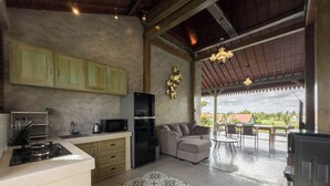 A kitchen with a gas stove, microwave, and refrigerator, a sofa, and a dining area with chairs. - Uma Nawasena Ubud (Ubud)