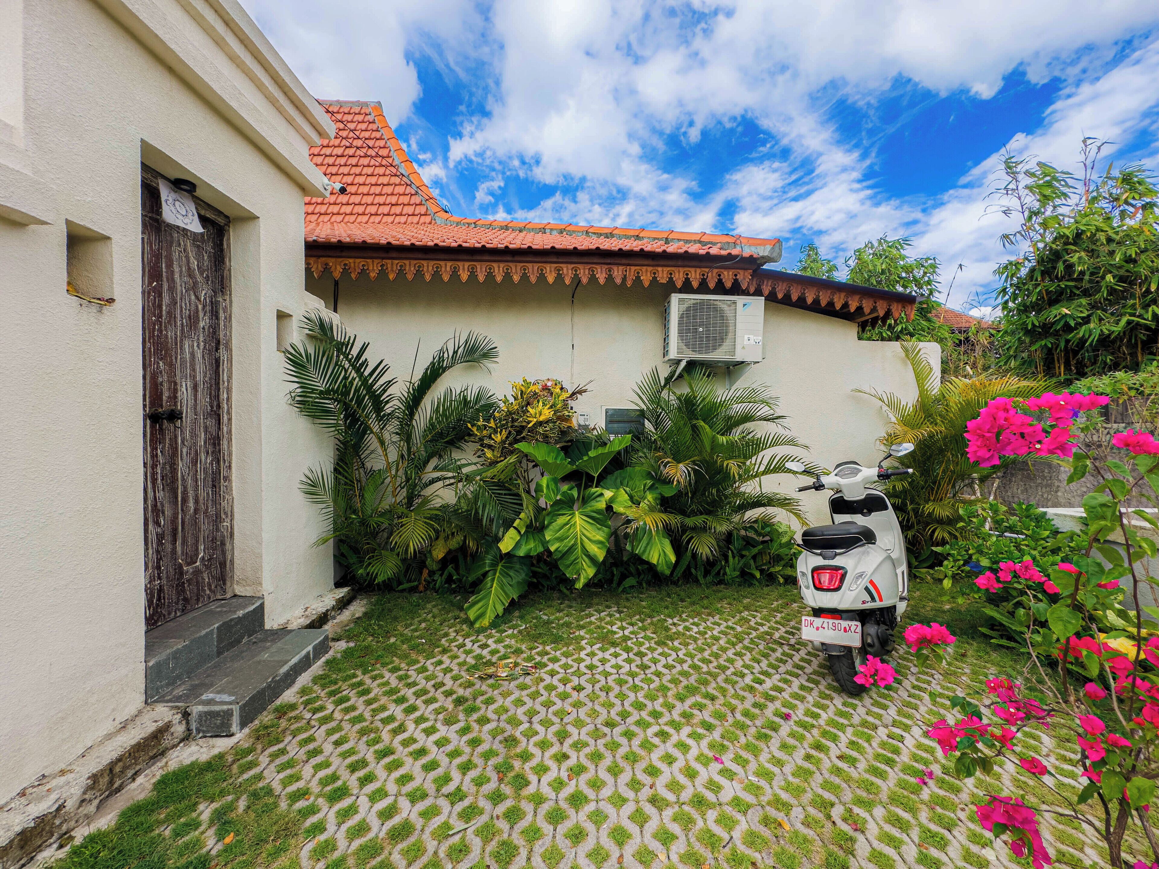 A courtyard with a tiled floor, a scooter, and lush greenery.