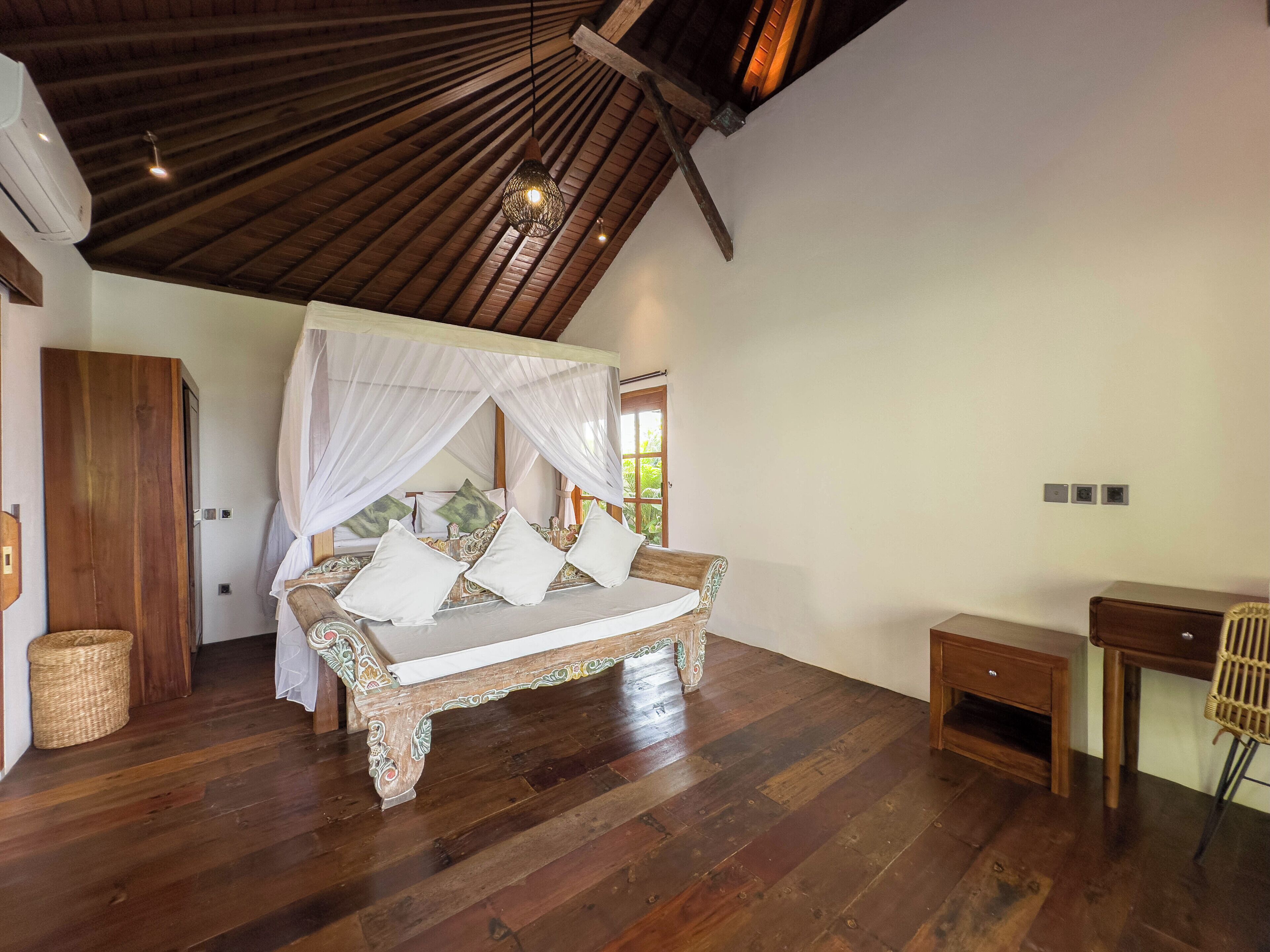 A bedroom with a wooden ceiling, a canopy bed, a wooden desk, and a wicker chair.