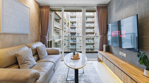A modern living room with a leather sofa, a round coffee table, and a large flat-screen TV displaying 'NETFLIX'. - Laeta by Kozystay - Paskal (Bandung)
