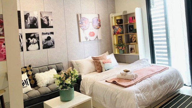 A modern hotel room with a large bed, a sofa, a small table with a vase of flowers, and a wall with framed pictures.