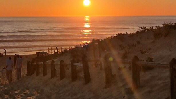 Una playa al atardecer con gente caminando por la orilla.