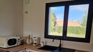 Una cocina con armarios blancos, encimera de madera, microondas, cafetera y ventana con vistas a una casa y follaje.