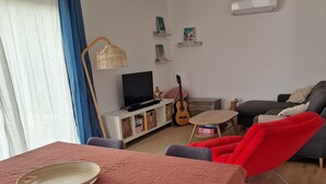 Una sala de estar con una cama, un televisor, una guitarra y un sillón rojo.