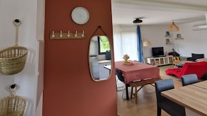 Una sala de estar moderna con comedor, una cocina visible a través de una puerta abierta y un espejo grande en la pared.