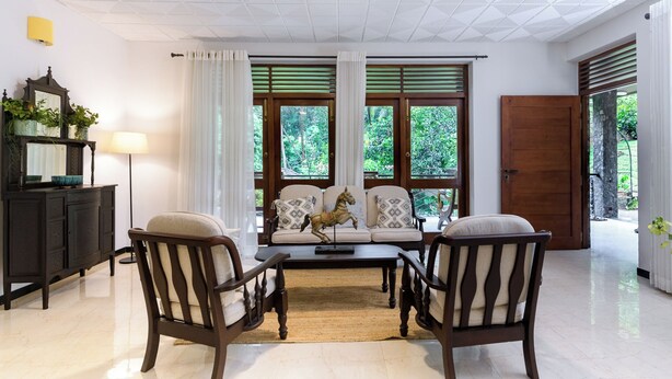 Une pièce comprenant un canapé, deux fauteuils, un meuble en bois et une grande fenêtre avec des rideaux.