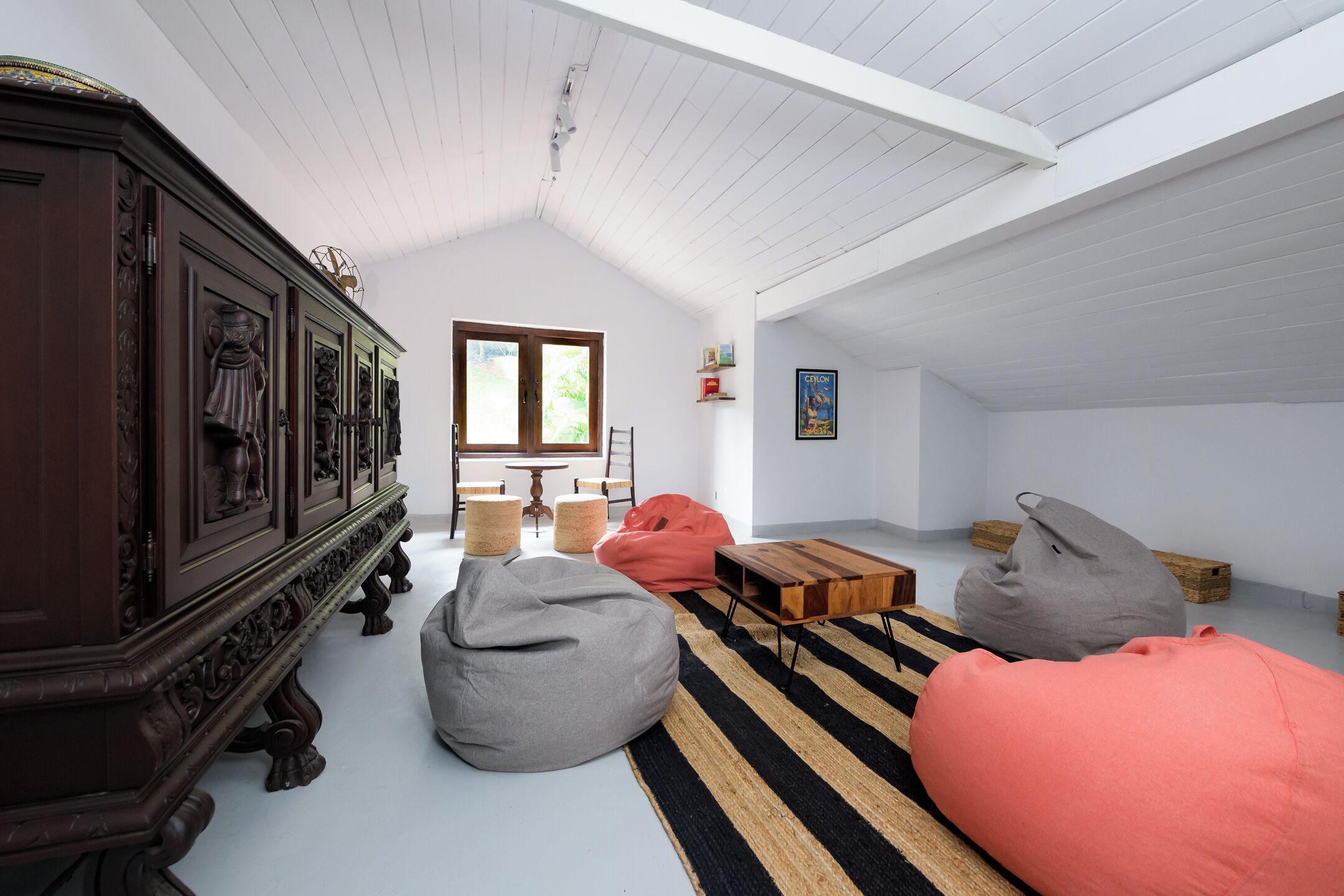 A spacious loft with high ceilings, a large wooden cabinet, and a cozy seating area with bean bags and a striped rug.