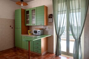 A kitchen with green cabinets, a microwave, and a window with sheer curtains. - Sea View Penthouse - Apulia Houses & Flats (Giovinazzo)