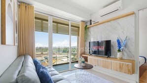 A modern living room with a grey sofa, a flat-screen TV, and a large window with a view of the city. - Jatayu by Kozystay - Paskal (Bandung)
