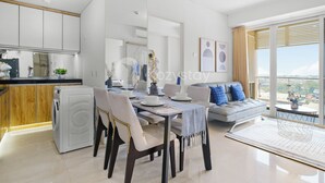 A modern living room with a dining area, a sofa, and a view of the city. - Jatayu by Kozystay - Paskal (Bandung)
