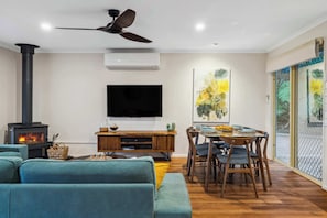 Ein Wohnzimmer mit Fernseher, Kamin, Deckenventilator, Esstisch und Stühlen.
