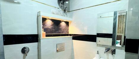 A modern bathroom with a toilet, sink, and mirror. There is a towel rack and a towel dispenser.