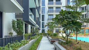 A modern residential building with a central pathway, surrounded by greenery and a swimming pool.