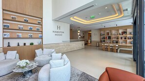 A modern hotel lobby with a reception desk, seating area, and a bookshelf with various items.