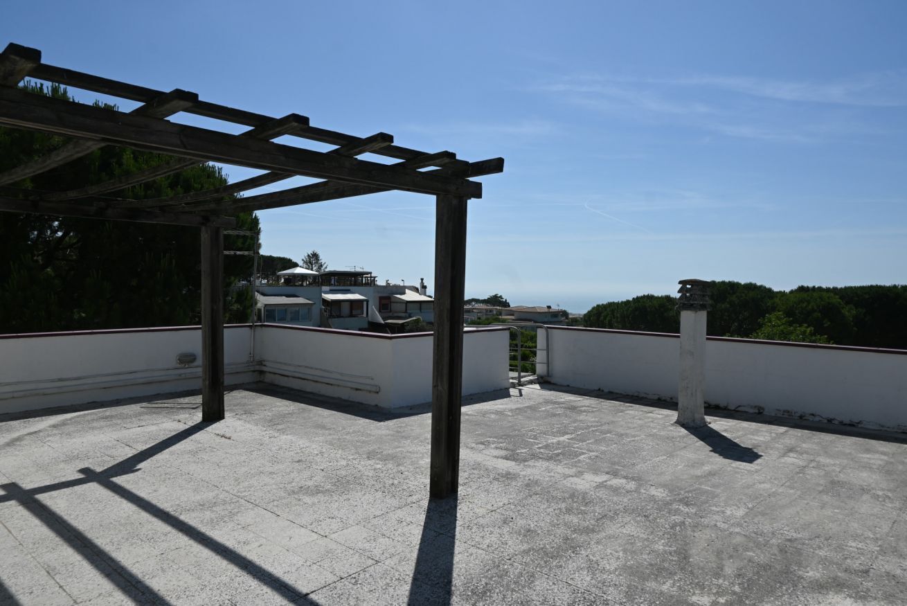 Eine Dachterrasse mit einer Pergola, ein weißes Gebäude im Hintergrund und klarer Himmel.