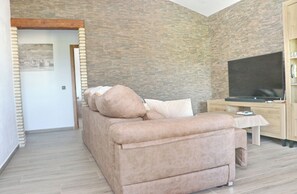 Una sala de estar moderna con un sofá beige, un televisor de pantalla plana y un mueble de entretenimiento de madera.